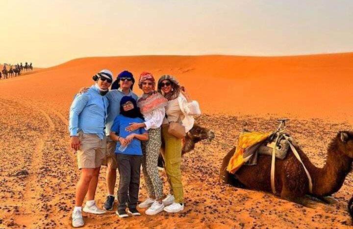 a group of people standing in the desert with a camel at ERG MERZOUGA SAHARA CAMP in Merzouga