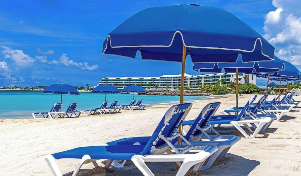a row of chairs and an umbrella on a beach at Beachfront Condo in Simpson Bay, SXM - 2BR 2BA in Simpson Bay
