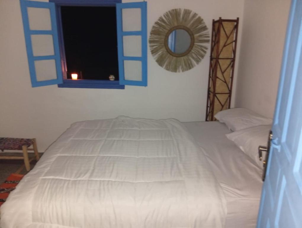 a bedroom with a white bed with a blue window at Sharing is caring Taghazout in Taghazout