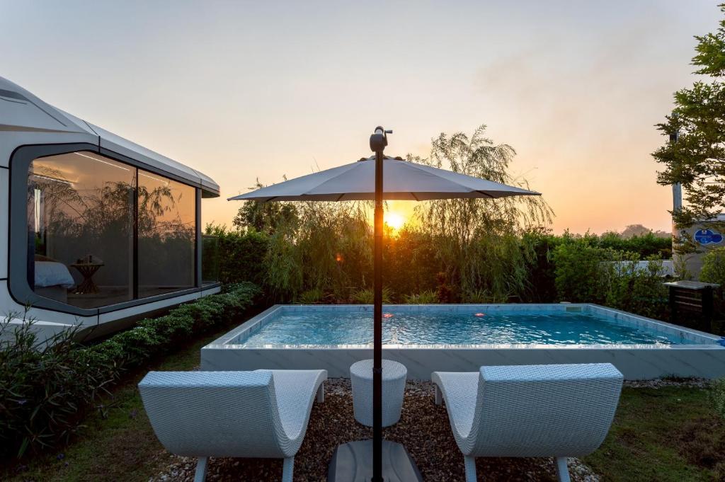 a swimming pool with two chairs and an umbrella at Nx Space พลูวิลล่า in Nakhon Nayok