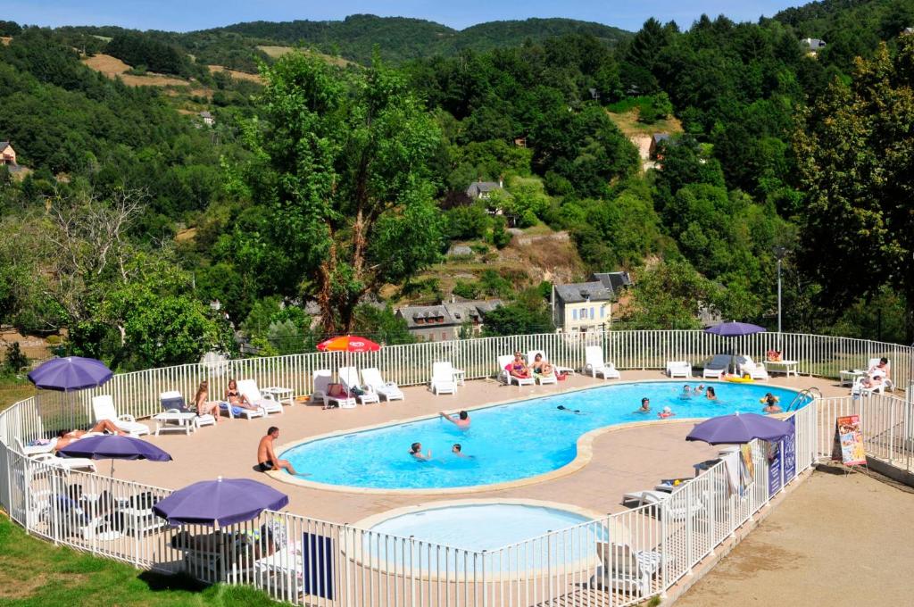 a large swimming pool with people sitting in chairs and umbrellas at Résidence Goélia Les Gorges de la Truyère in Entraygues-sur-Truyère