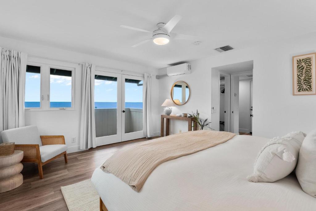 a white bedroom with a bed and a chair and windows at Kona Kai Ocean View Suite in Kailua-Kona