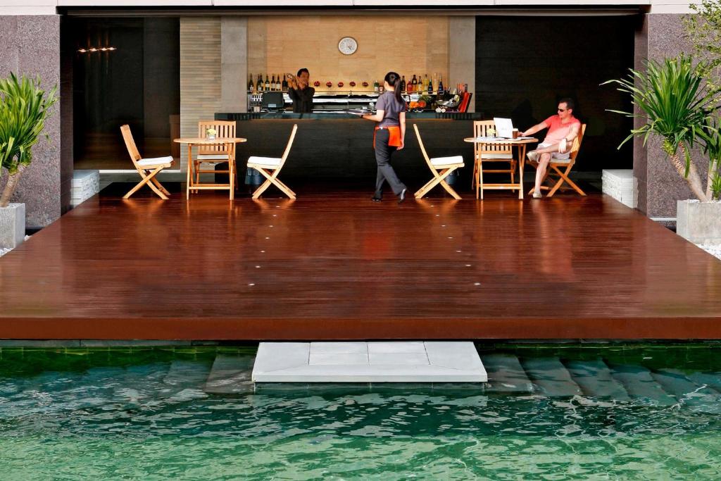A narrow pool fronts a raised wooden deck with a bar and outdoor tables.
