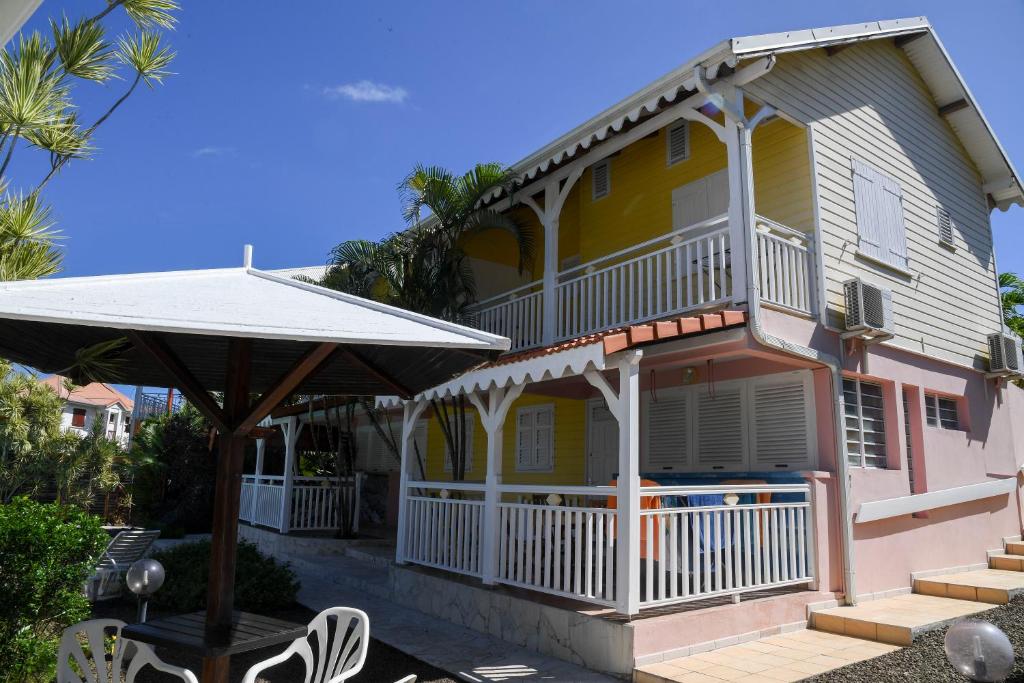 a yellow and pink house with a porch and an umbrella at L'escapade in Sainte-Anne