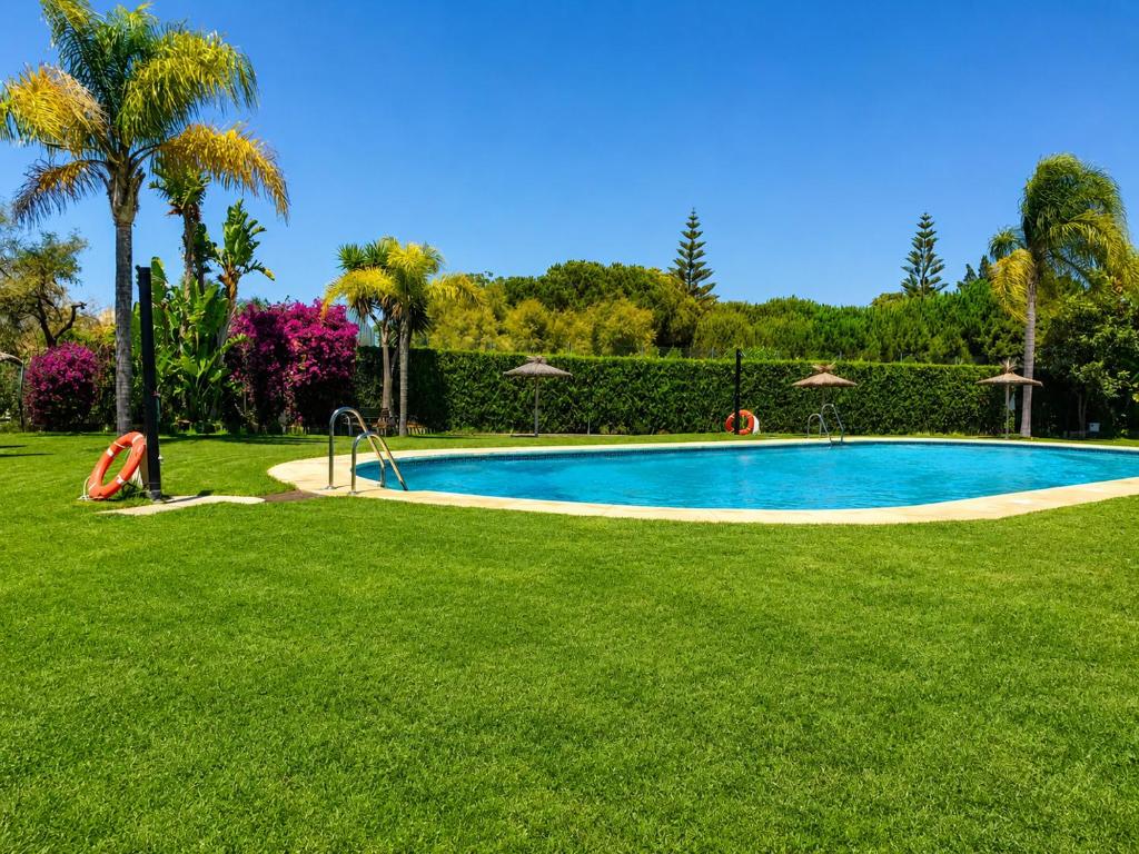 a swimming pool in the middle of a green lawn at Casa Denver in El Rompido