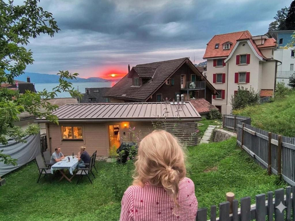 Eine Frau sitzt auf einem Zaun und schaut auf ein Haus. in der Unterkunft Chalet Oz Vitznau with Lake Lucerne Views in Vitznau