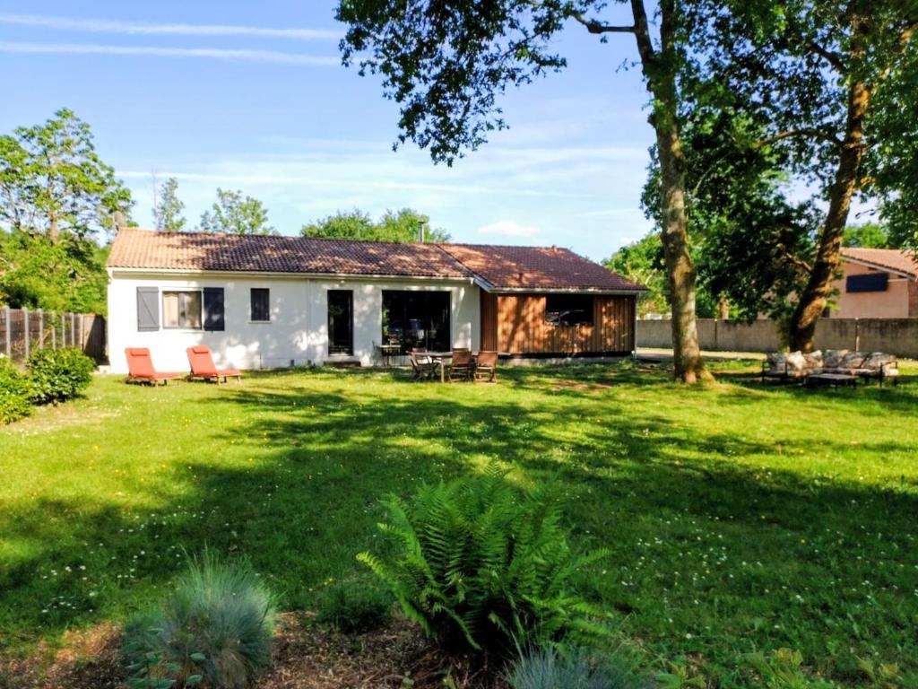 a small white house with two red chairs in a yard at Maison paisible en lisière de foret 9 personnes in Le Temple