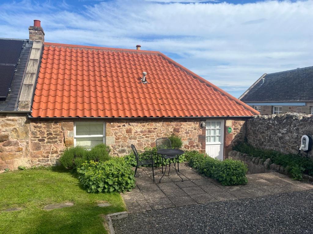 a house with an orange roof with a table and chairs at The Wee Bothy at East Lothian Cottages in Lennoxlove