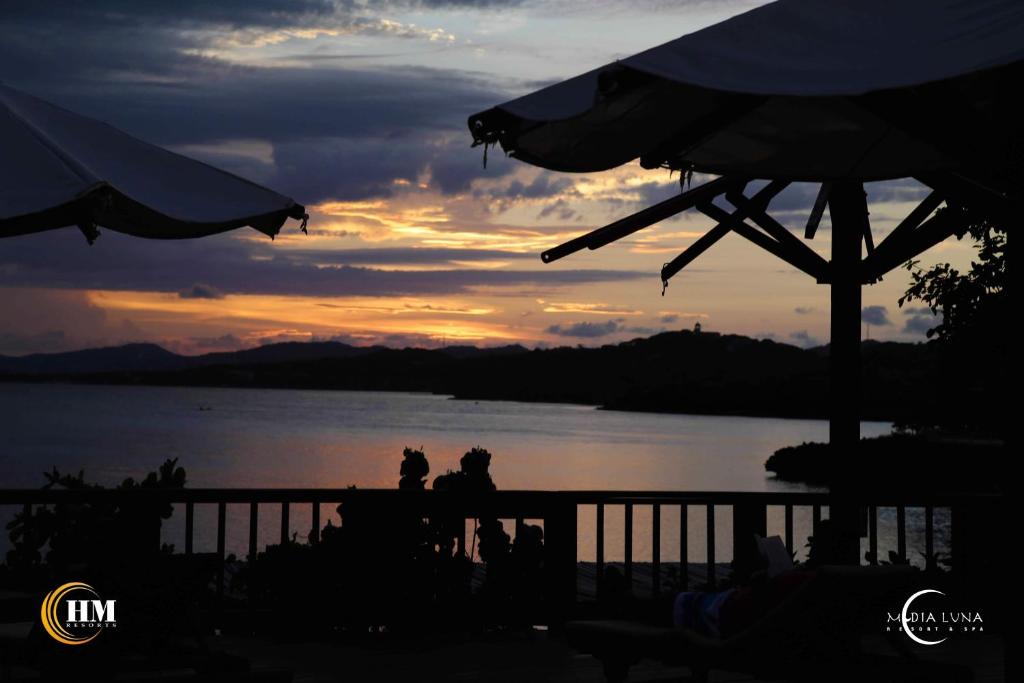 two people standing on a fence near the water at sunset at Media Luna Resort & Spa in First Bight