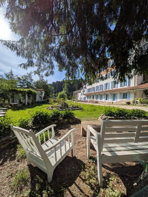 two white benches sitting under a tree next to a building at Les Contes in Fougax-et-Barrineuf