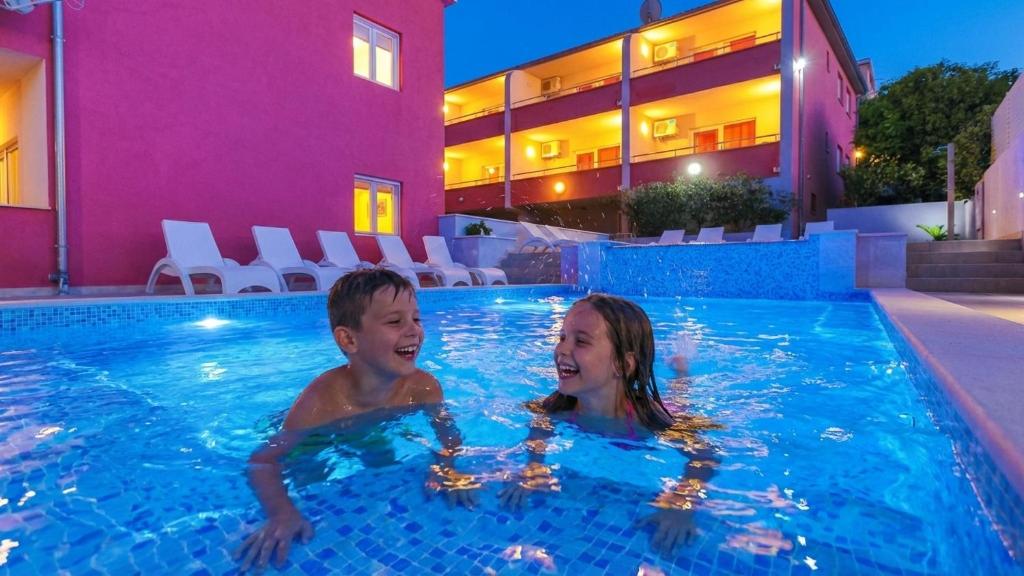 a boy and a girl swimming in a swimming pool at Apartments Stina & Villa Ina in Seget Vranjica