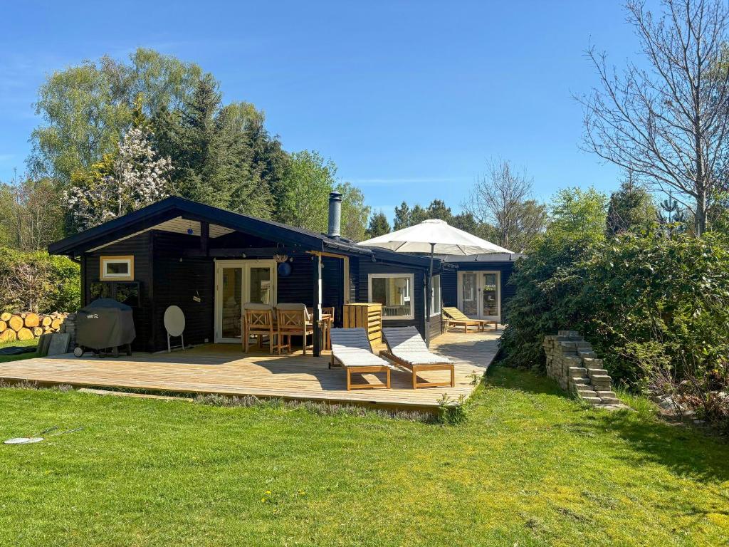 a small cabin with a deck with chairs and an umbrella at Summerhouse Close To Nature And Beach in Rørvig