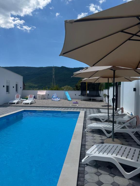 a swimming pool with chairs and umbrellas next to at Hubby Resort in Mostar