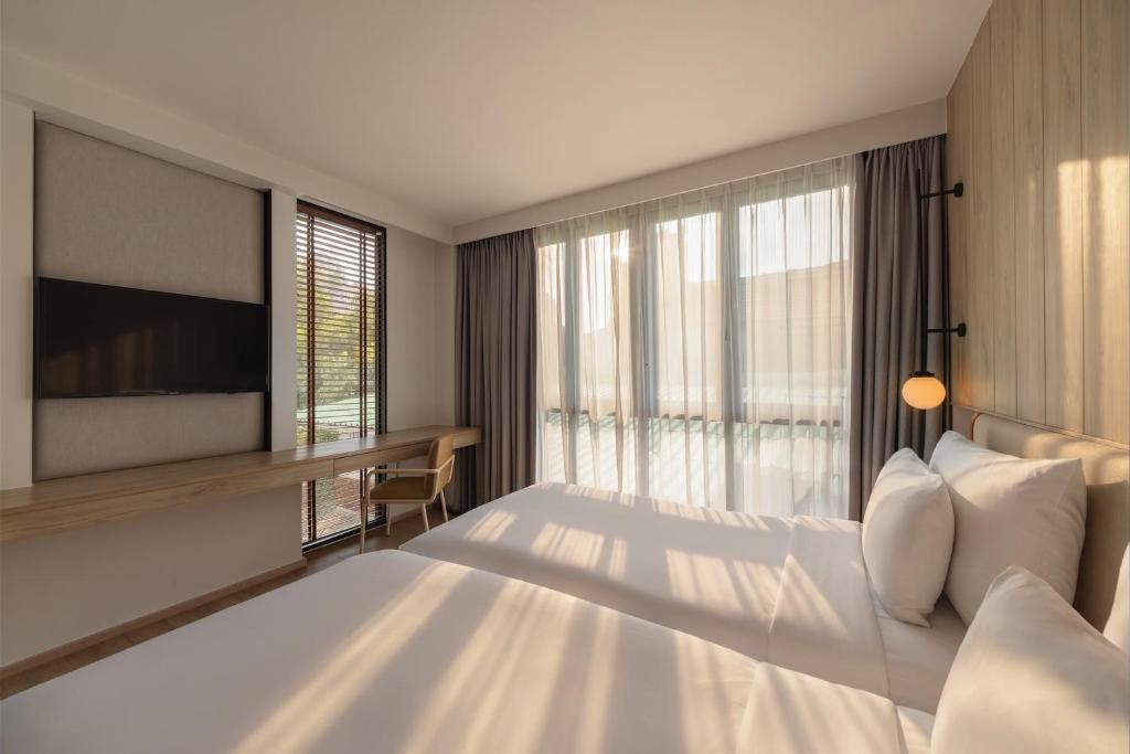 A sunlit king room with a small desk, television and sheer-curtained window.