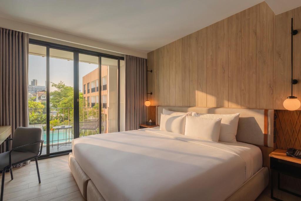 A sunlit bedroom opening toward a balcony or glass-fronted exterior area, with a king-size bed and wood-lined walls.