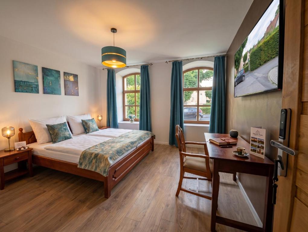 a bedroom with a bed and a desk and two windows at Templomdomb Apartmanház in Tapolca