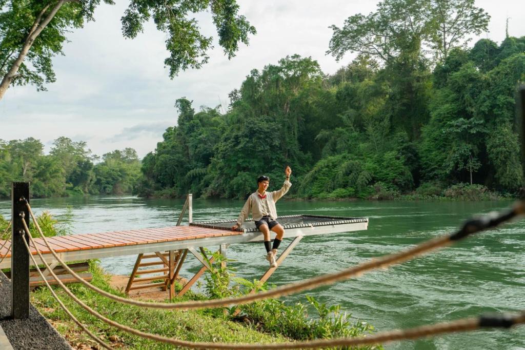 a man sitting on a dock on a river at Puprai Tarnnarm Resort in Thong Pha Phum
