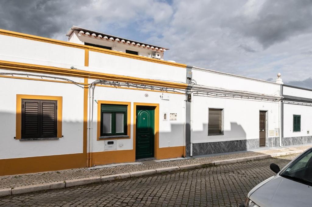a white building with green doors on a street at Casa da Muralha in Beja