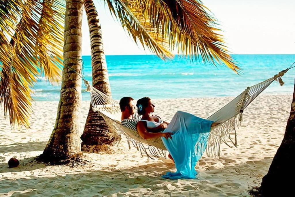 two people sitting in a hammock on the beach at DELUXE OCEAN view VILLAS & Apartments with POOL - PLAYA LOS CORALES, BBQ, SPA in Punta Cana