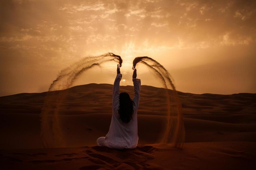 a woman sitting in the desert with her hands in the air at Grand Dunes Luxury Camp in Merzouga