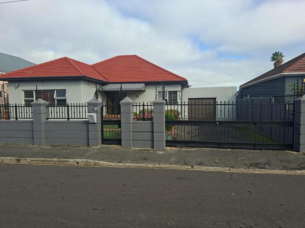 a fence in front of a white house with a red roof at Le Cape Nest Guest House in Parow