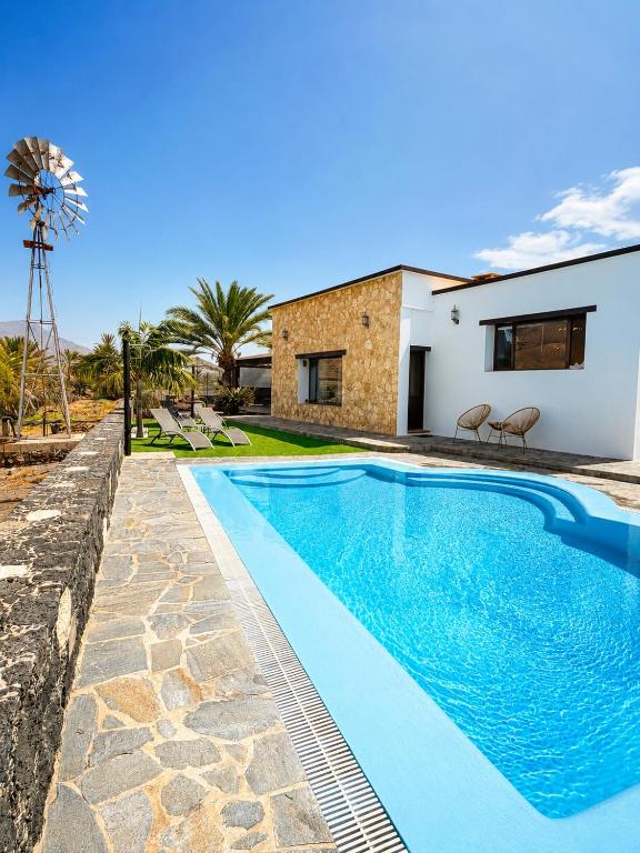 a swimming pool in front of a house with a windmill at Villa El Valle - Piscina climatizada in Tarajalejo