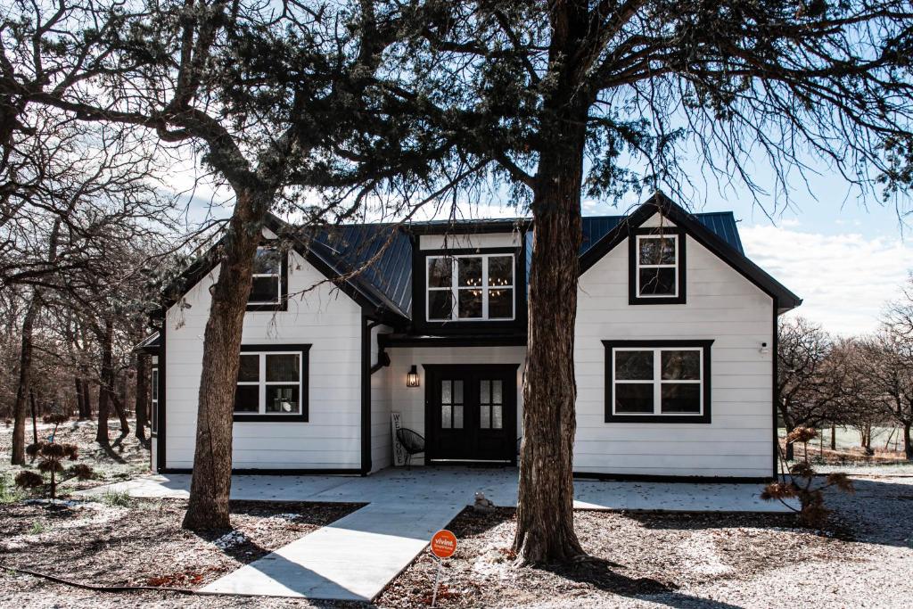 a white house with a black roof and two trees at Made with Love in Thackerville