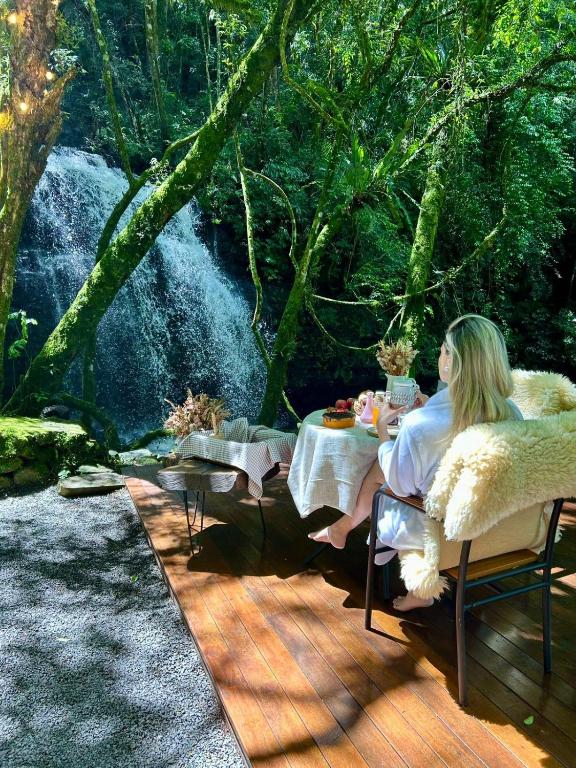 a woman sitting at a table on a deck at Lumine Cabanas- Chalé na Serra Gaúcha in Farroupilha