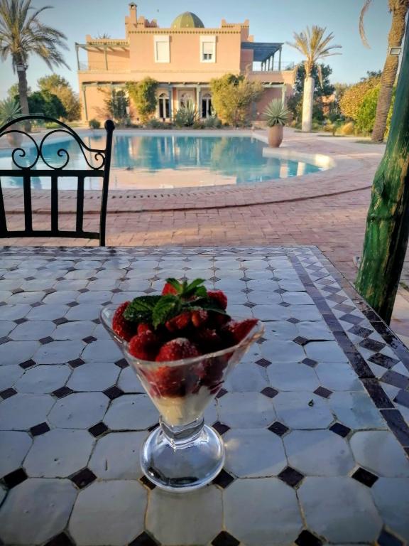 a bowl of strawberries on a table in front of a pool at Les jardins bleus in Taroudant