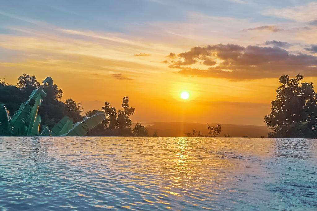 a infinity pool with a sunset in the background at Dudu Cottage Nusa Penida in Nusa Penida