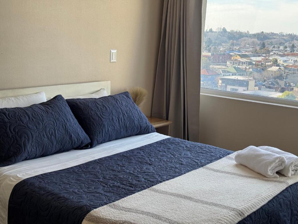 a bed with a blue and white blanket and a window at Alto Arrayán in Osorno