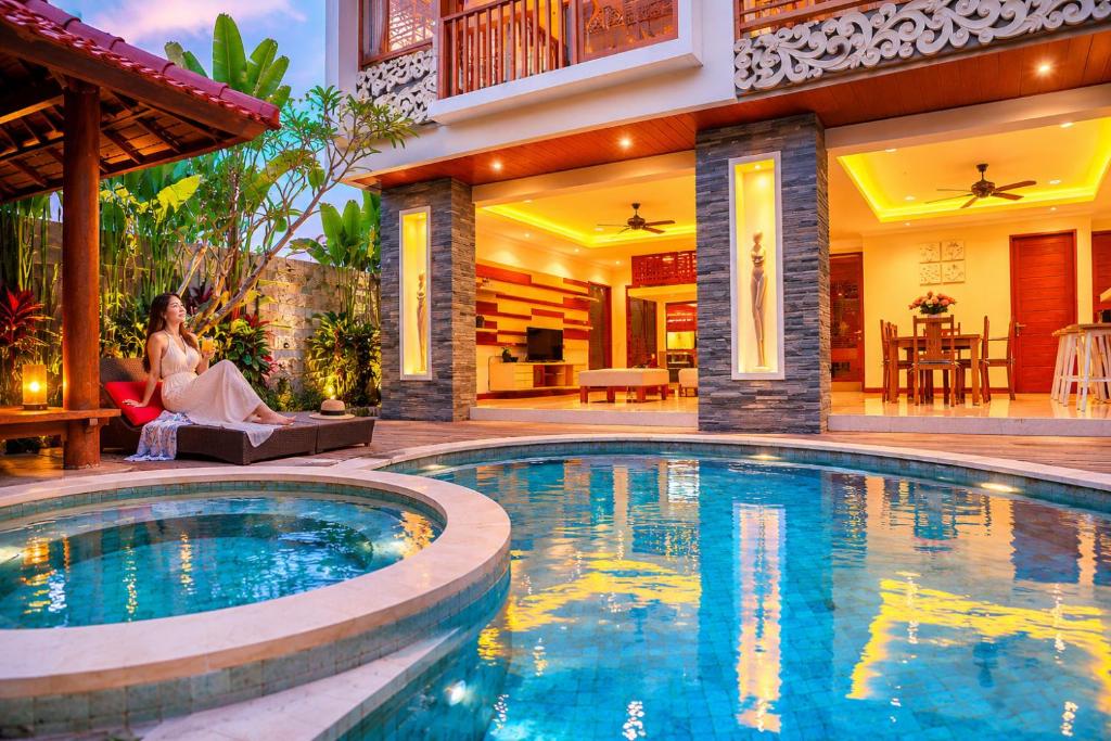 a woman sitting on a couch next to a swimming pool at Villa Suzuki 2 Seminyak in Seminyak