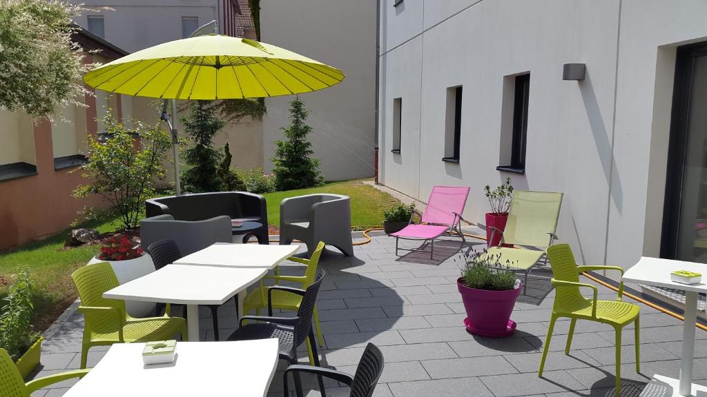 um pátio com mesas e cadeiras e um guarda-sol amarelo em ibis Styles Montbéliard em Montbéliard