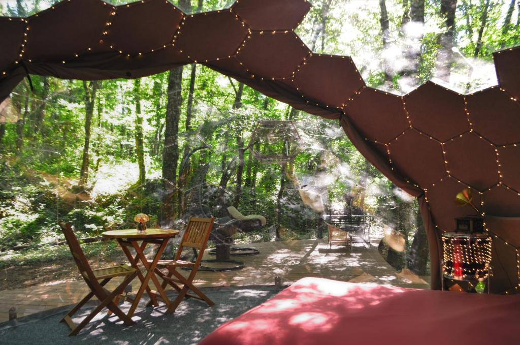 a patio with a table and chairs in the woods at Ô Pays Des Bois - Bulles et logements insolites en pleine nature - Adults Only in Parmilieu