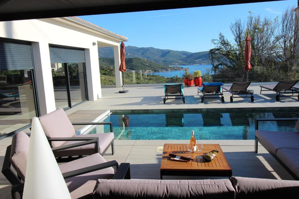 a patio with a pool and chairs and a table at Villa d exception piscine privée 200m2 10 pers RESTONICA Les Terrasses de Ruppione in Pietrosella