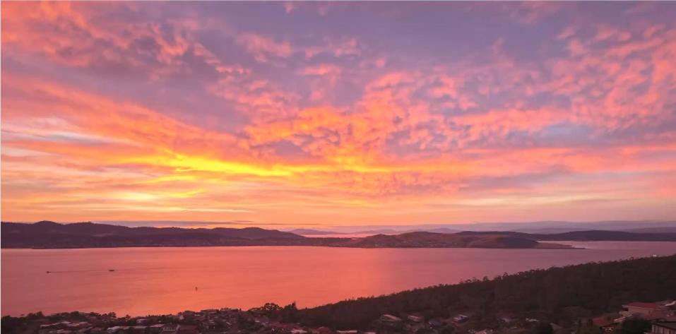 a sunset over a large body of water at Sandy Bay Sunrise Panorama House in Hobart