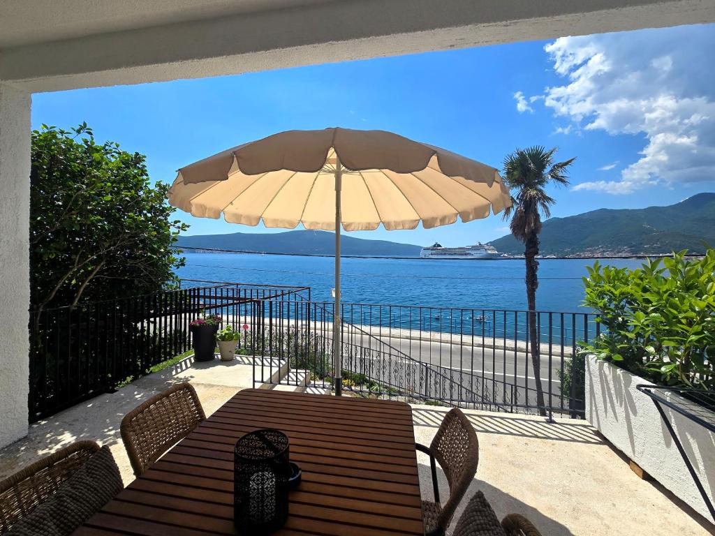 a wooden bench with an umbrella in front of the ocean at Apartmani Nikolić "Na pjeni od mora" in Tivat