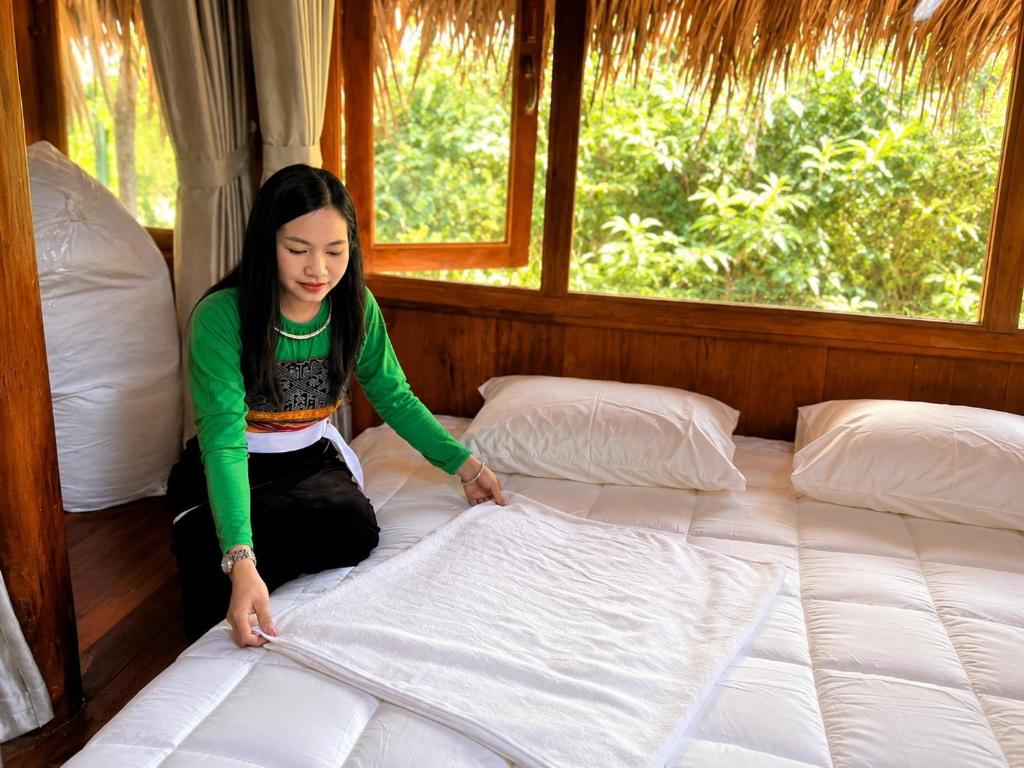 a woman is making a bed in a room at Mai Chau Ecohouse in Mai Châu