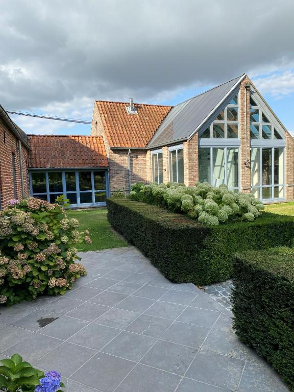 a brick house with a greenhouse and some bushes at Maison l'amitié in Ellezelles