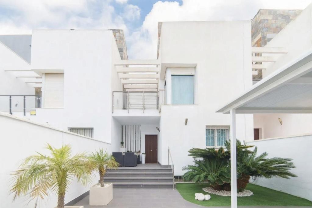 a white house with palm trees in the courtyard at Chalet Adosado en Playa La Barrosa in Novo Sancti Petri