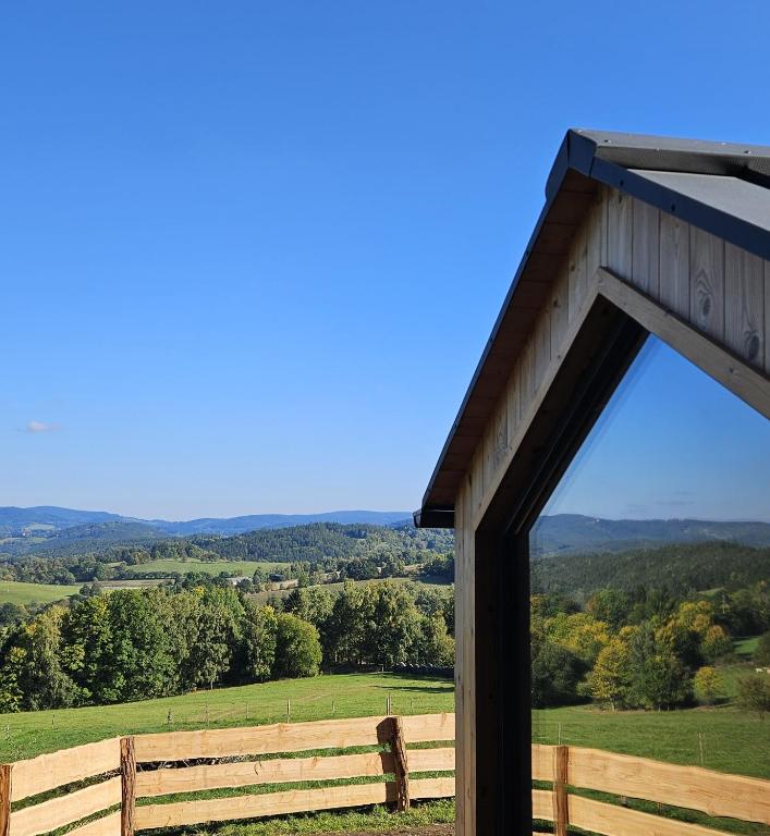 a barn with a view of a field and a fence at Glamping Šumava in Hartmanice