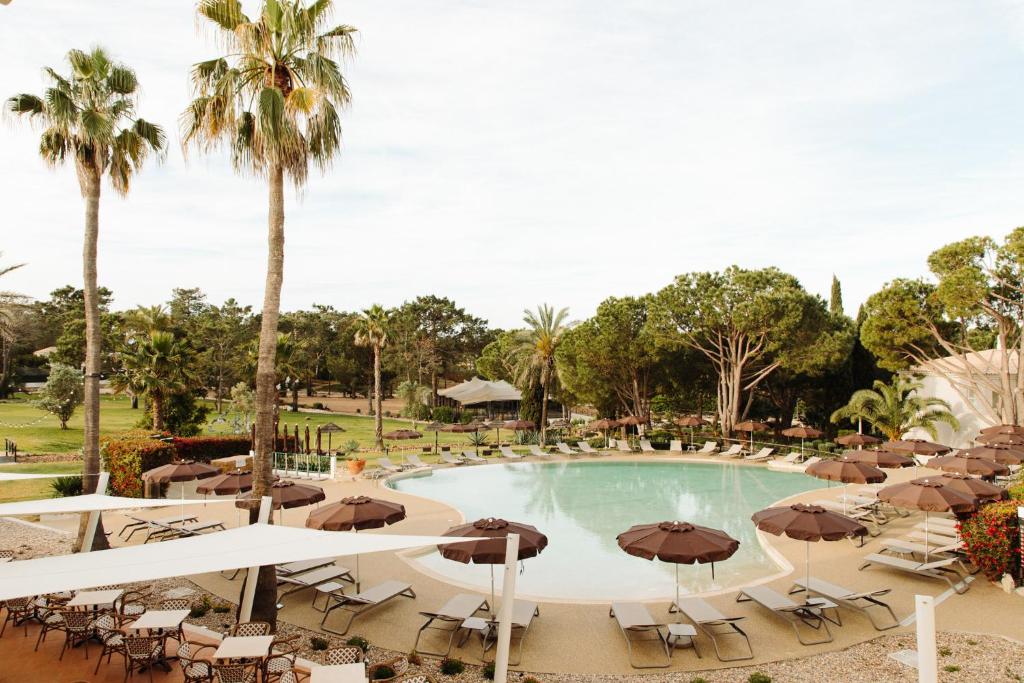 a swimming pool with umbrellas and chairs and trees at Vale d'El Rei Hotel & Villas in Carvoeiro