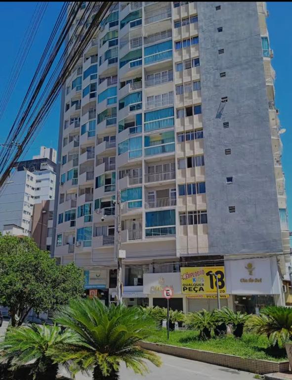 a tall building with palm trees in front of it at Apartamento Centro Guarapari in Guarapari