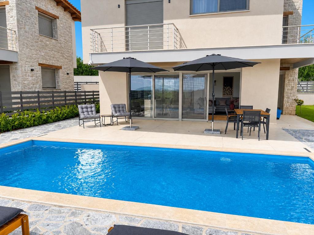 a swimming pool with chairs and umbrellas next to a house at Elysian View Lefkakia in Nafplio