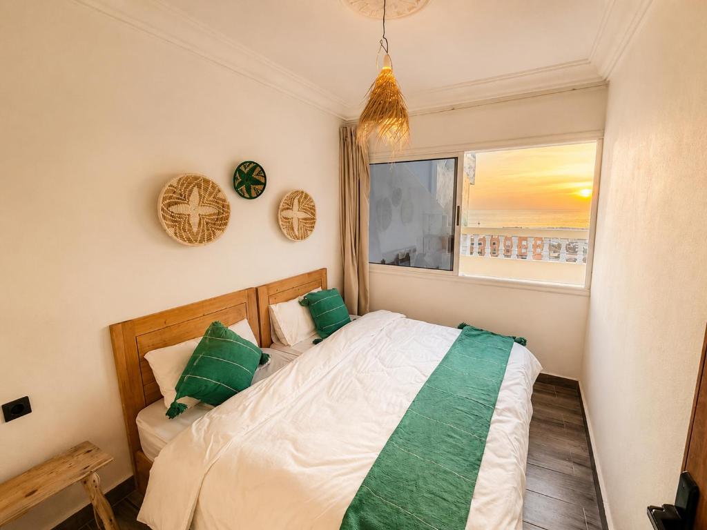 a bedroom with a bed with green pillows and a window at Happy Waves Morocco - Surf Hostel Tamraght in Tamraght Ou Fella
