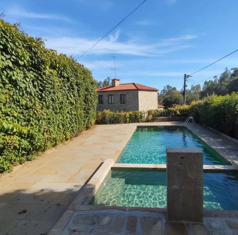 a swimming pool in a garden next to a hedge at Holly Country House in Paredes de Coura