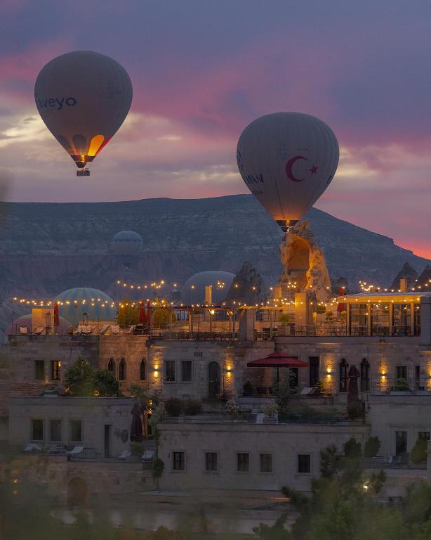 dwa balony na ogrzane powietrze latające nocą nad budynkiem w obiekcie Carus Cappadocia w Göreme