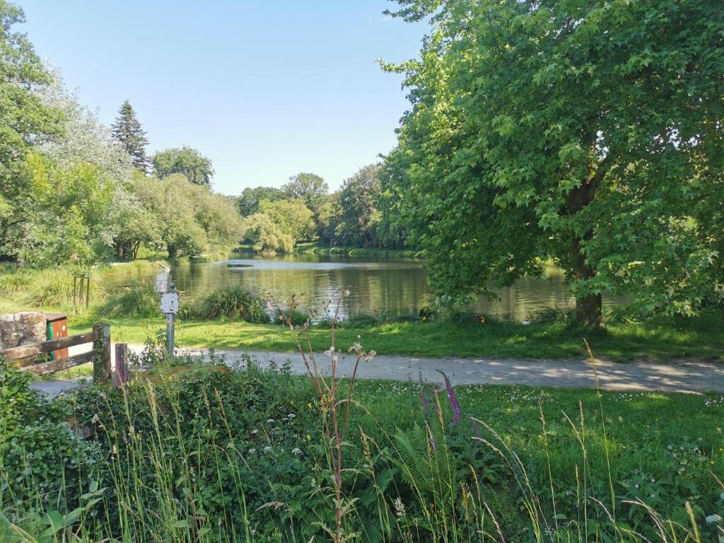 a lake in a park with a path next to it at Le Moulin in Saint-Nolff
