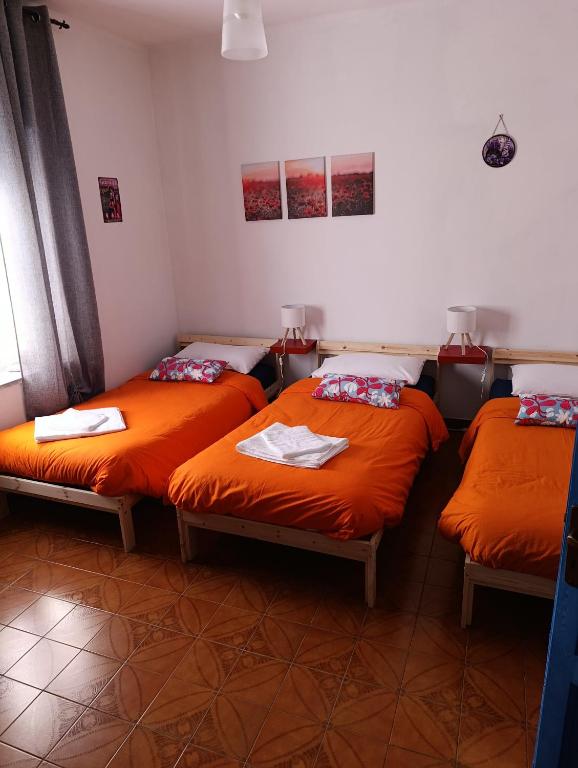 three beds in a room with orange sheets at Ël Sautafoss in Agliè