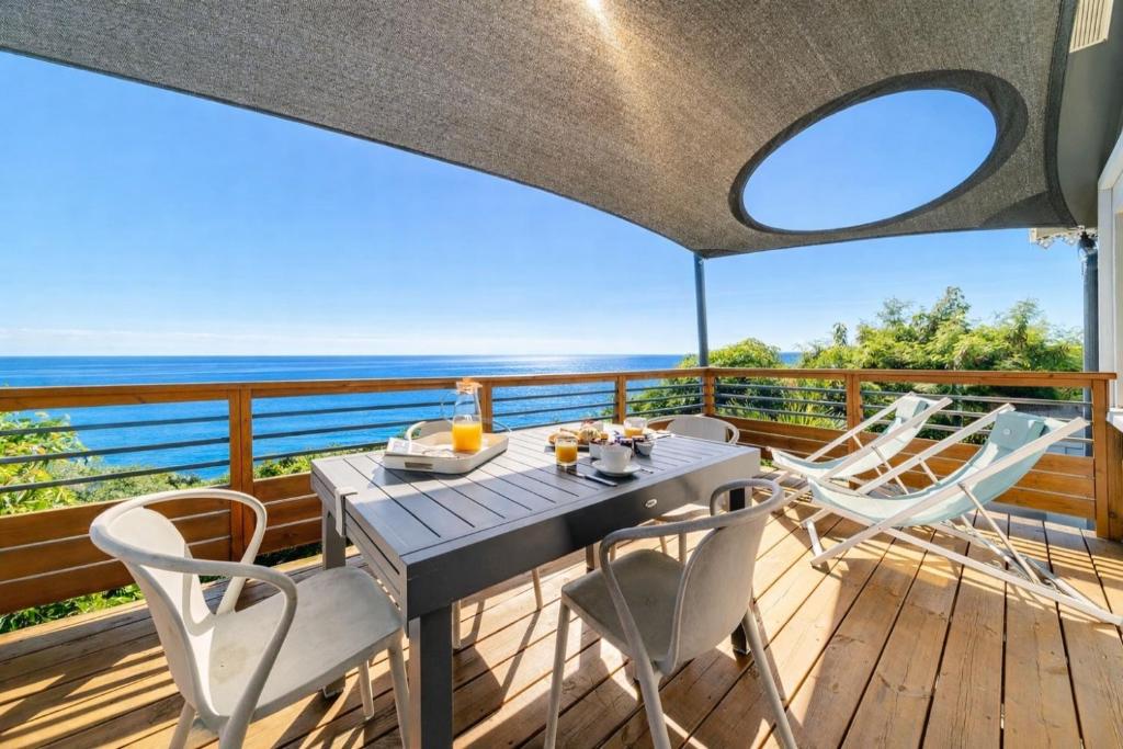 a table and chairs on a deck with a view of the ocean at Les Pailles en Queue - Vue mer - Appartements de Charme & Standing in Sainte-Marie